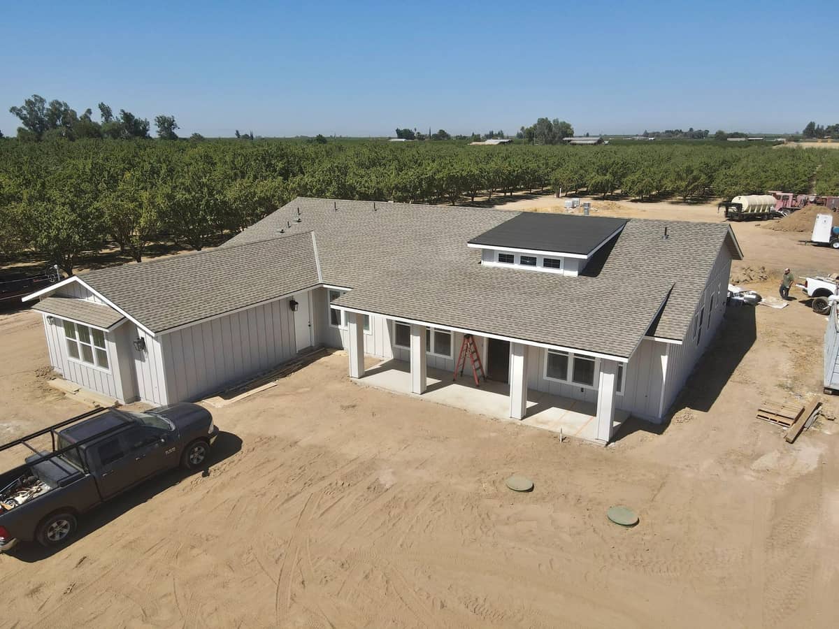 Custom home nearing completion on a dirt lot with an almond orchard behind it