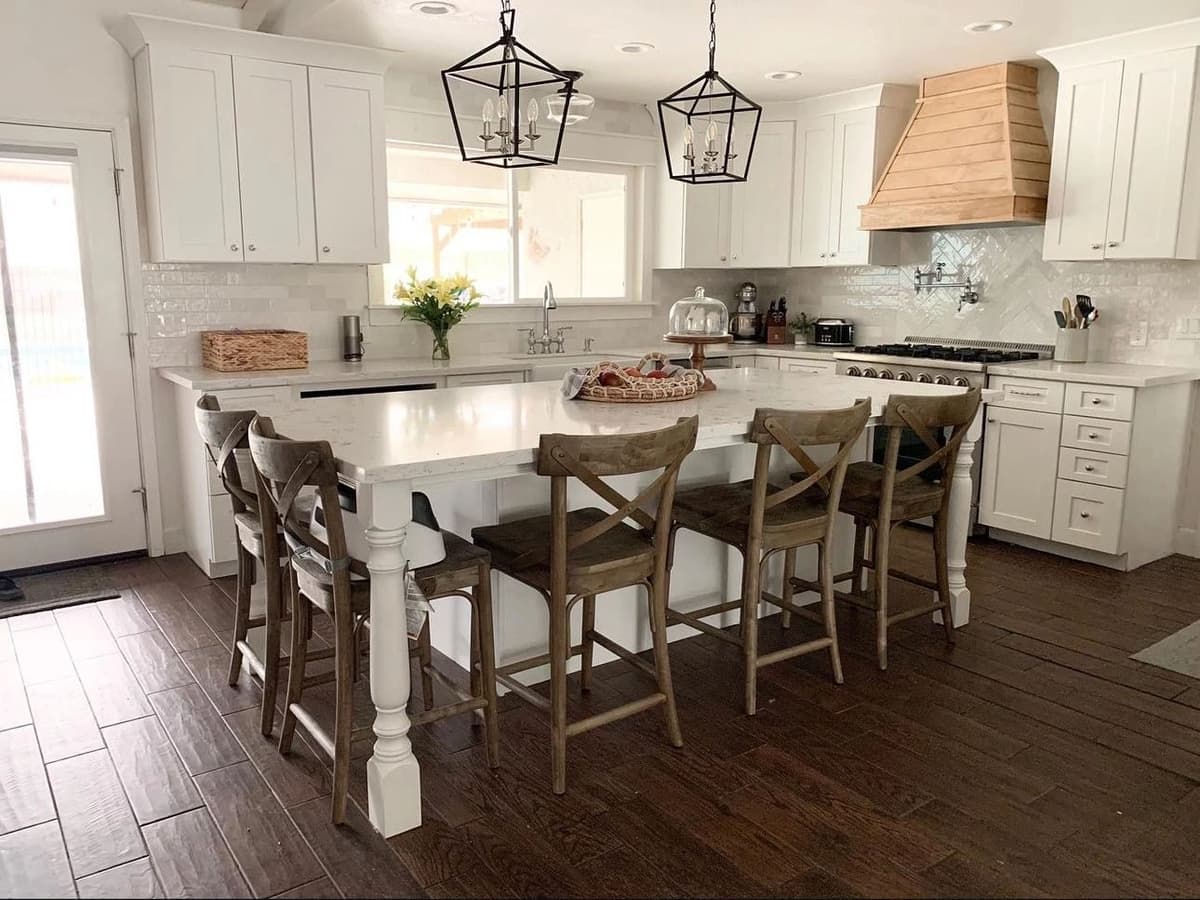 Finished custom kitchen with a large white island, wood bar stools, and a wood range hood